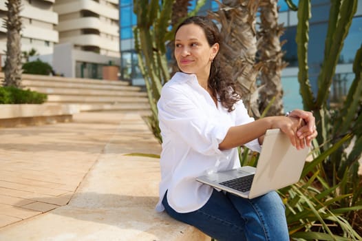 Beautiful mixed race young adult happy woman entrepreneur, freelancer, sales manager, business lady in white casual shirt, holding laptop and confidently looking aside. People. Career. Online job