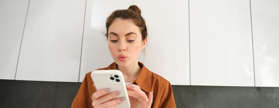 Portrait of young woman at home, looking with interest at smartphone screen, concept of online shopping, buying on mobile apps, picking something using application on phone.