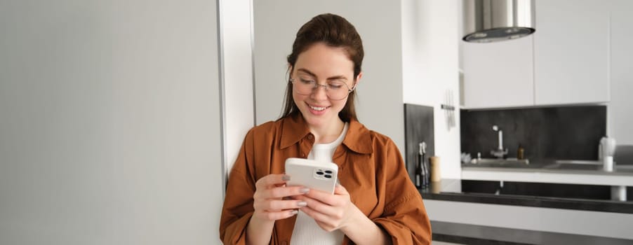 Beautiful woman checking social media while using smartphone at home. Smiling young female using mobile phone app and playing game, shopping online or reading news. Copy space.