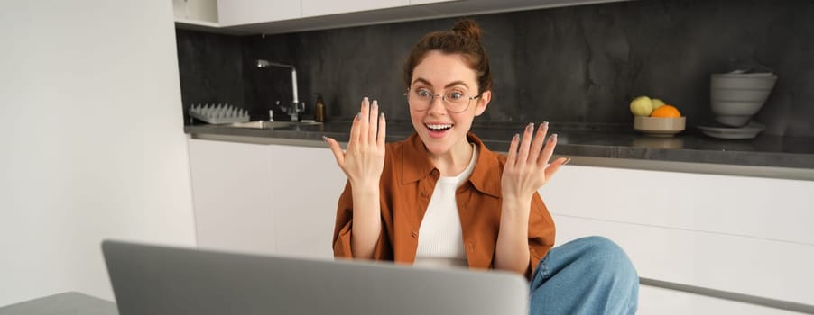 Portrait of surprised, happy woman in glasses, looking at laptop with amazed, excited face expression, positive reaction to big news.