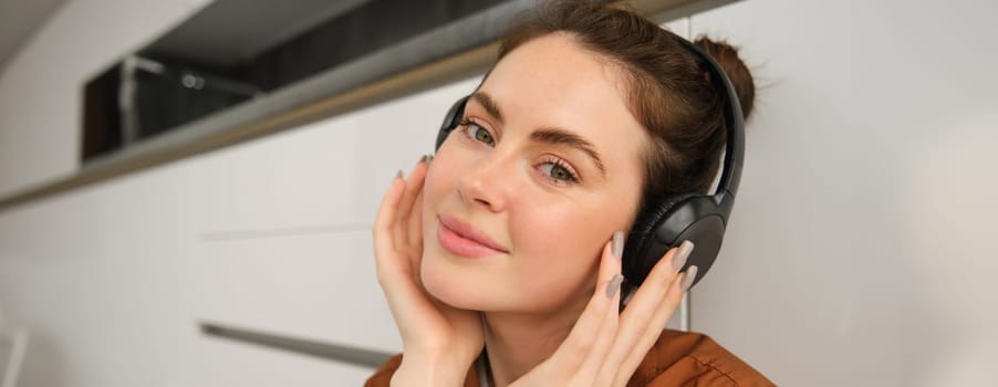 Portrait of smiling woman with headphones, listens to music, looks at camera.