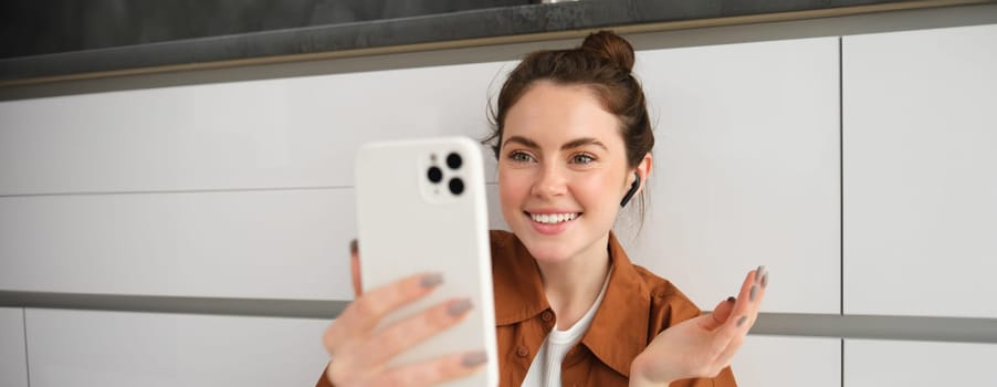Portrait of beautiful smiling woman, talking to friend on smartphone video chat, connects to online conversation on mobile app, sitting on kitchen floor.