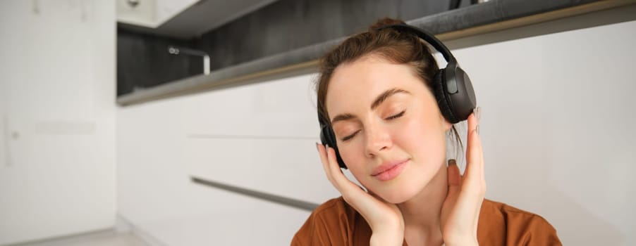 Close up portrait of happy, smiling young woman listens to music in wireless headphones, enjoys favourite song or melody in earphones.