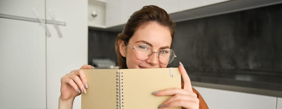 Close up portrait of young woman smiling, holding notebook, showing her planner.