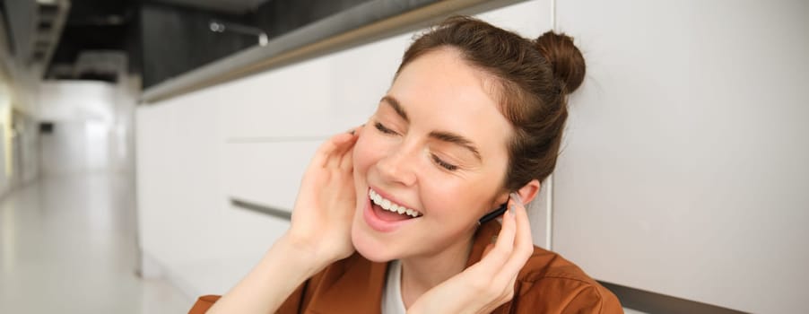 Close up portrait of girl enjoying listening to music in wireless earphones, smiling, wearing headphones, sitting at home.