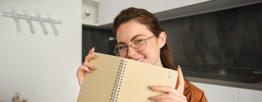 Close up portrait of young woman smiling, holding notebook, showing her planner.