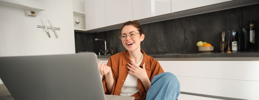 Portrait of carefree young woman, student with laptop sitting at home, talking with friend via video chat, connects to online conversation from computer, laughing and smiling.