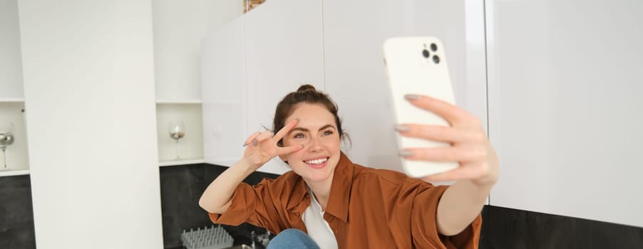 Portrait of beautiful young woman takes selfie on her smartphone, posing for photos, using filter app to take pictures for herself.