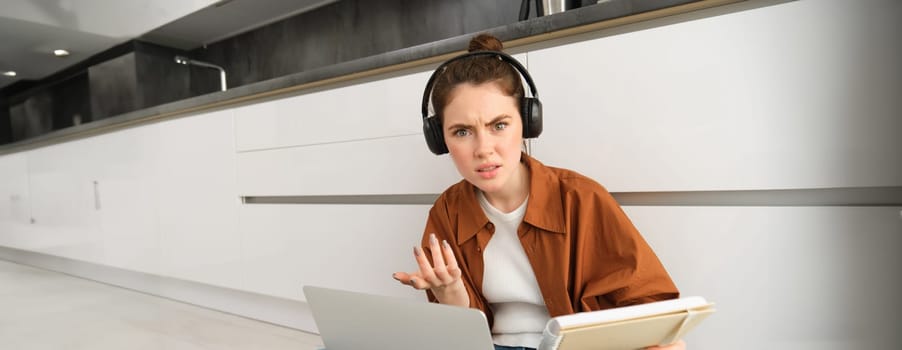 Confused and frustrated woman in headphones, student doesnt understand something while doing homework on laptop, looking annoyed at camera.