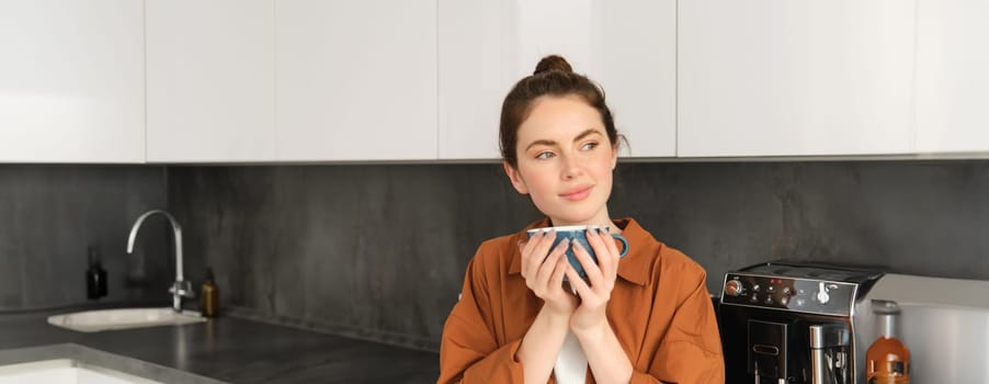 Close up portrait of beautiful, relaxed young woman, enjoying aroma of coffee, drinking cappuccino and smiling. Lifestyle and people concept