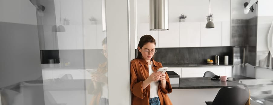 Portrait of cute young woman standing at home with smartphone, reading message on mobile phone, using application, order online, paying utility bill in app.