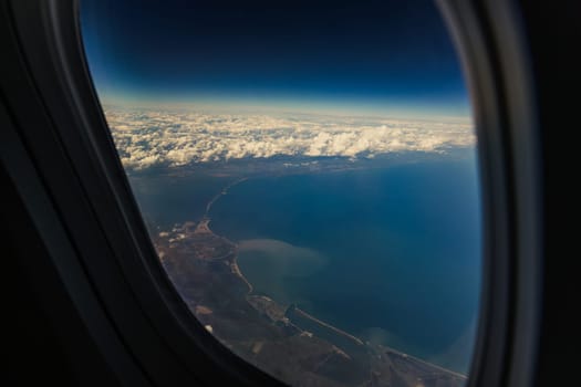 A beautiful view of the blue sea and a piece of land with white clouds through the airplane window in the evening summer, close-up side view.