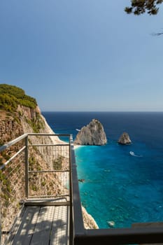 Beautiful view of the observation deck and two rocks in the blue sea with passing boats near the beach coastline on a sunny summer day, close-up side view.