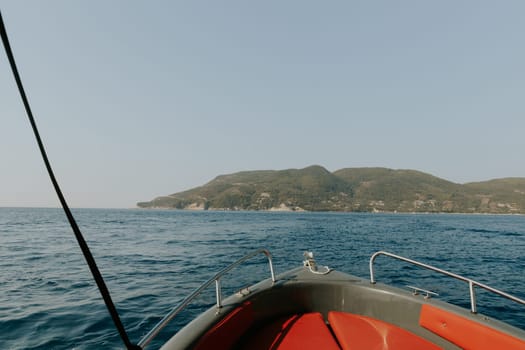 Beautiful panoramic view of a green mountain island in the blue sea with the bow of a boat on a sunny summer day, close-up side view.