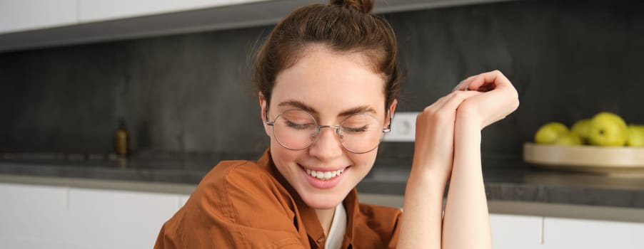 Close up portrait of young woman at home, sitting in glasses in the kitchen. Lifestyle and modern people concept