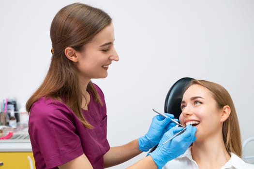 Female dentist doing treatment for patient, holding dental tools in modern dental clinic.