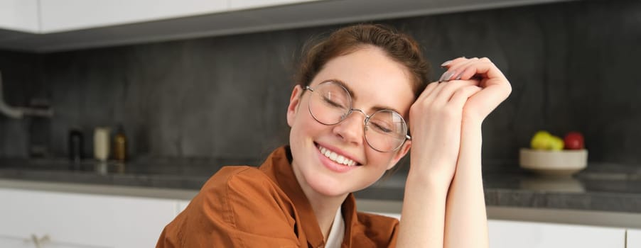 Close up portrait of brunette woman in glasses, beautiful female model sitting in kitchen, laughing and smiling, express carefree, positive emotion.
