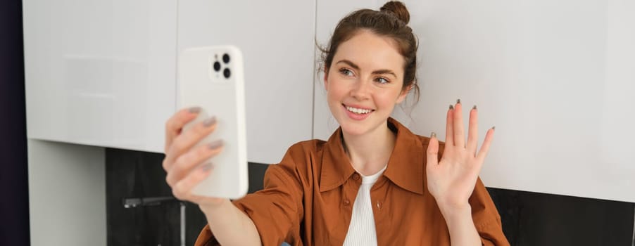 Lifestyle shot of young woman video chatting, using smartphone app to talk online, records herself for social media blog, looks happy.