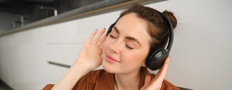 Close up portrait of happy, smiling young woman listens to music in wireless headphones, enjoys favourite song or melody in earphones.