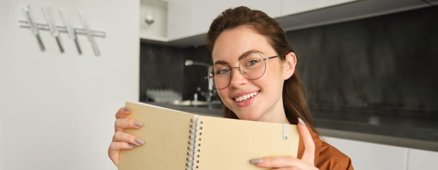 Close up portrait of young woman smiling, holding notebook, showing her planner.