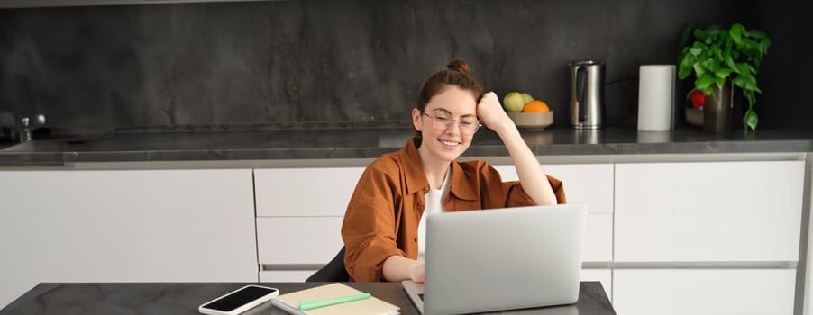 Portrait of woman freelancer, programmer working from home. Female student or business owner sitting with laptop in kitchen.