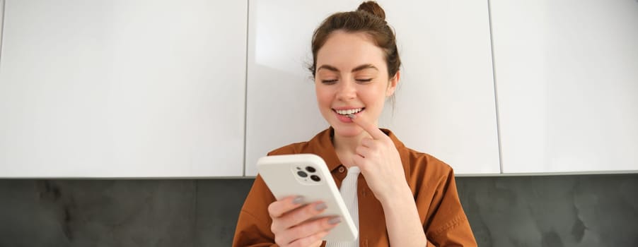 Portrait of beautiful young modern woman with smartphone, smiling while looking at mobile phone screen, concept of buying online, shopping from home.