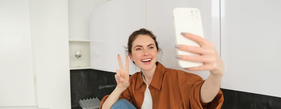 Portrait of beautiful young woman takes selfie on her smartphone, posing for photos, using filter app to take pictures for herself.