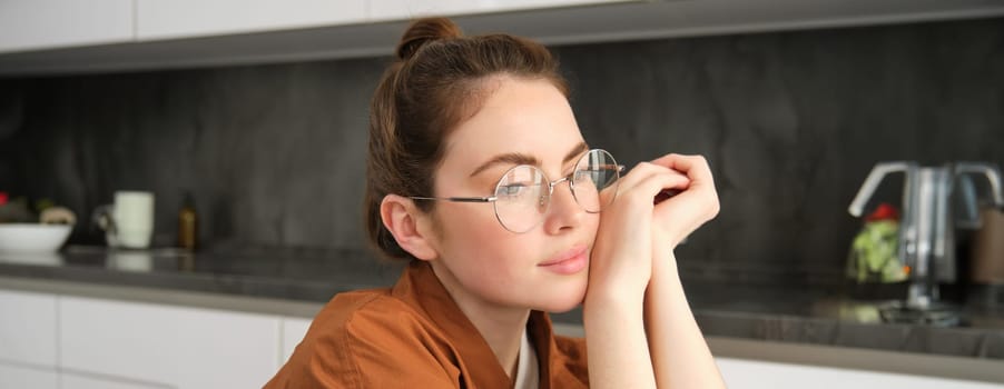 Close up portrait of young woman at home, sitting in glasses in the kitchen. Lifestyle and modern people concept