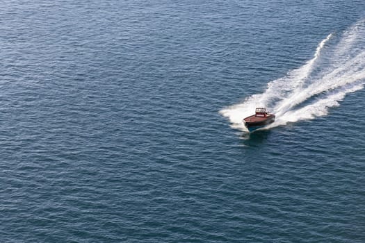 A red boat sailing in a tranquil body of water, with powerful jet streams trailing behind it