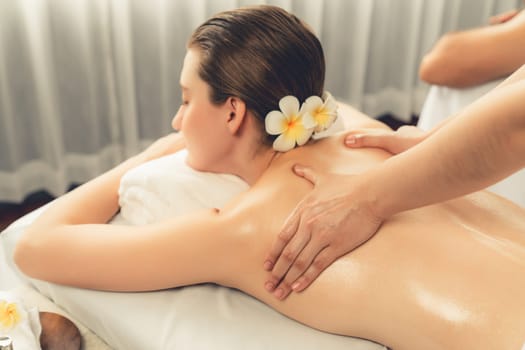 Caucasian couple customer enjoying relaxing anti-stress spa massage and pampering with beauty skin recreation leisure in day light ambient salon spa at luxury resort or hotel. Quiescent