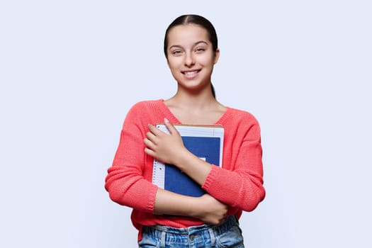 Portrait of girl, teenage high school student on white studio background. Smiling female student 15, 16 years old with books notebooks looking at camera. Adolescence, education, knowledge concept