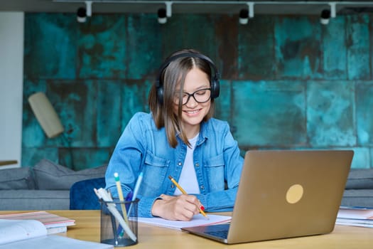 Female university student with headphones having online lesson lecture, video conference, sitting at table at home, looking laptop screen. Internet technologies in education e-learning virtual classes