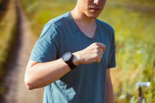 A young male athlete puts on a heart rate monitor and smart watch before jogging in nature. A man monitors his pulse and is engaged in a healthy running outdoor.
