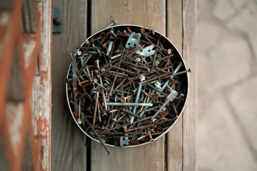 Old vintage nails in a round box lie on the porch of a wooden country house, top view. Old things for workshop and recycling and creative work.