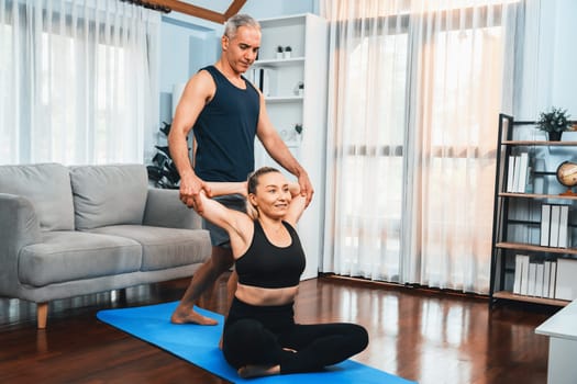 Happy active senior couple in sportswear being supportive and assist on yoga posture together at home. Healthy senior man and woman lifestyle with yoga exercise. Clout