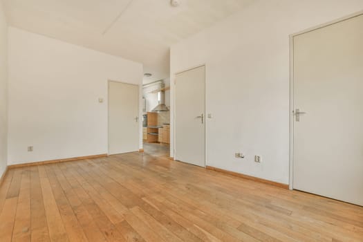 an empty living room with wood flooring and white walls on either side of the room, there is a kitchen in the corner