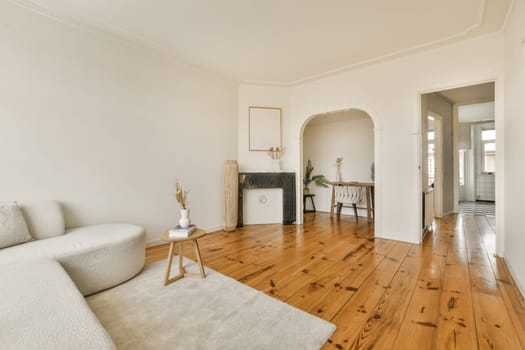 a living room with white walls and wood flooring in the center of the room is an arched doorway that leads to another room