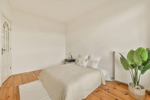 a bedroom with white walls and wood flooring in the room, it has a large green plant on the side of the bed