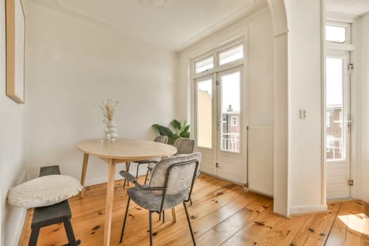 a dining table and chairs in a room with white walls, hardwood flooring and large windows looking out onto the street