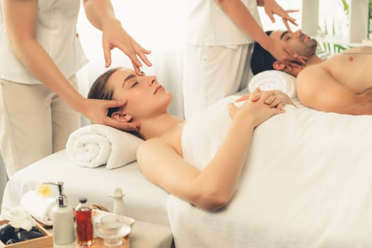 Caucasian couple enjoying relaxing anti-stress head massage and pampering facial beauty skin recreation leisure in dayspa modern light ambient at luxury resort or hotel spa salon. Quiescent