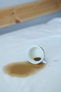 cup of coffee spilled on gray white bed .