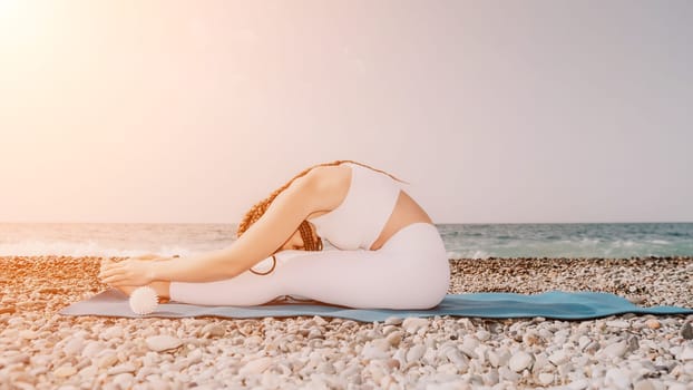 Woman yoga sea. Well looking middle aged woman with braids dreadlocks in white leggings and tops doing stretching pilates on yoga mat near sea. Female fitness yoga routine concept. Healthy lifestyle