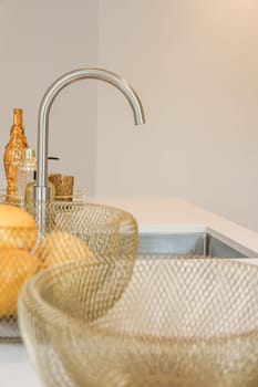 some oranges in a bowl on a kitchen sink with water running down the drainer and fauced