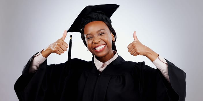 Graduation, thumbs up and woman or student success with celebration, education and learning or college achievement in studio. Portrait of happy african graduate with like emoji on a white background.