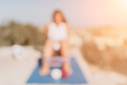 Middle aged well looking woman with black hair doing Pilates with the ring on the yoga mat near the sea on the pebble beach. Female fitness yoga concept. Healthy lifestyle, harmony and meditation.