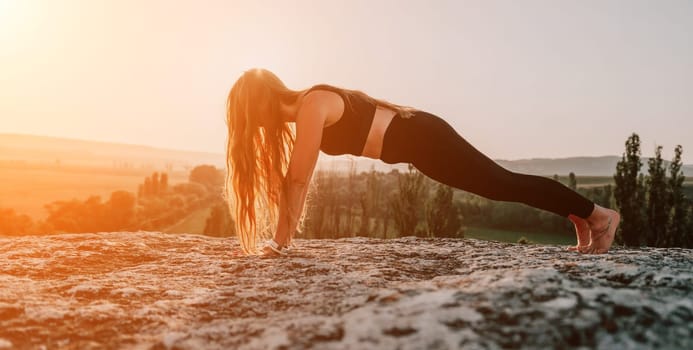 Well looking middle aged woman with long hair, fitness instructor in leggings and tops doing stretching and pilates on the rock near forest. Female fitness yoga routine concept. Healthy lifestyle.