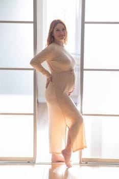 A pregnant woman in a long beige dress stands in profile between the folding doors