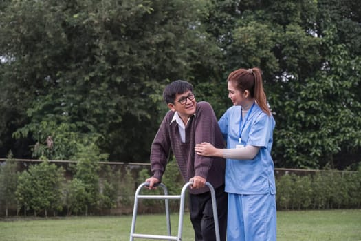 Asian female caregiver helps senior man walk A senior using a walker is assisted by a nurse at home. A nurse helps an elderly patient at a nursing home. Elderly care and healthy lifestyle.