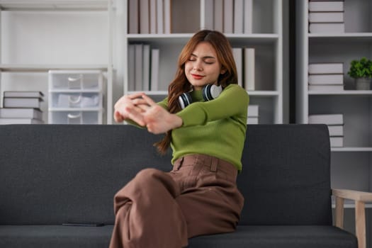 Asian woman listening to music while sitting on the sofa Attractive young woman wearing headphones feels happy spending free time at home and enjoying weekend activities at home..