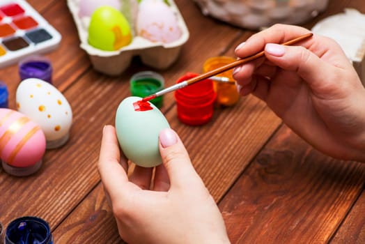 A woman with a tassel paints Easter eggs. Preparing decorations for Easter, creativity with children, traditional symbols. Preparing for Easter.